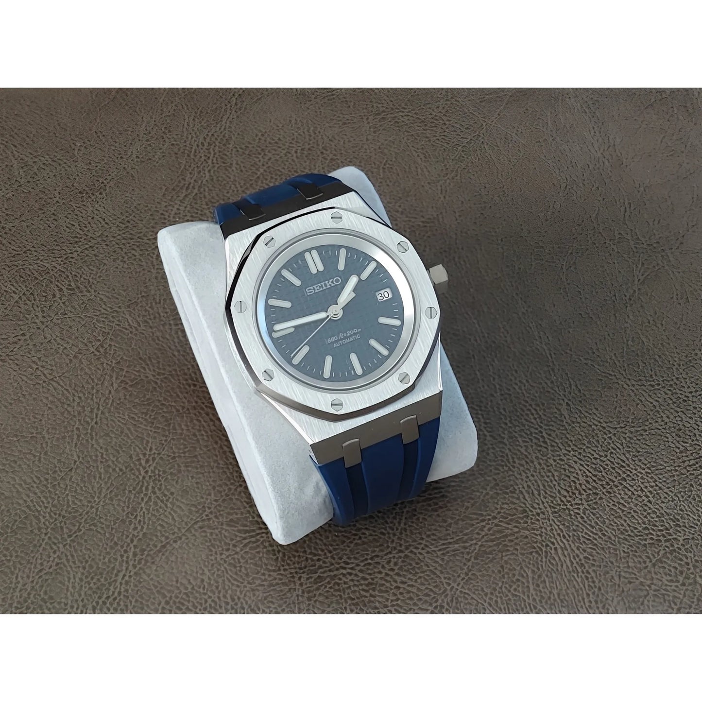 Seiko NH35 Royal Oak watch with navy blue dial, silver octagonal bezel, and blue rubber strap on white cushion.