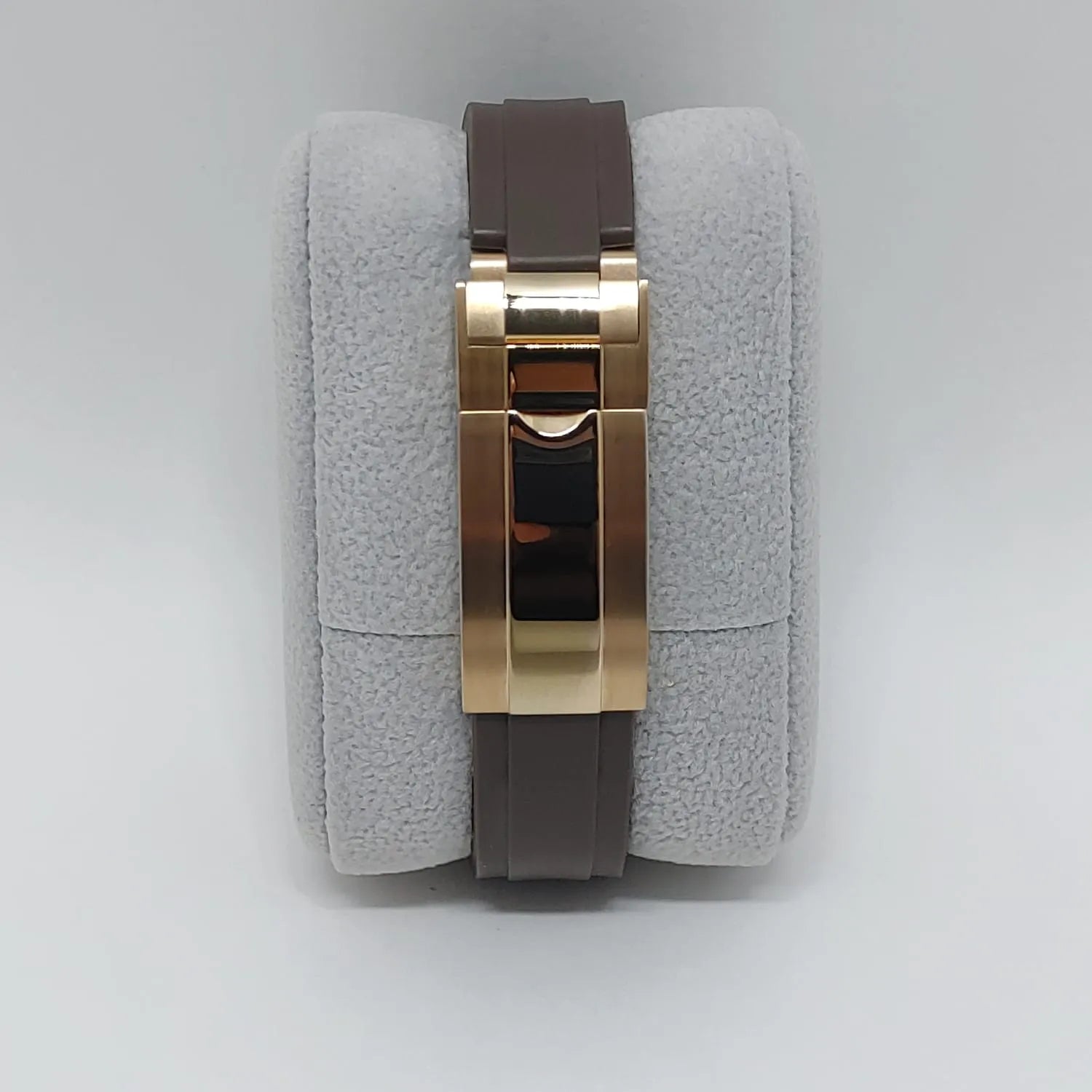 Brown leather watch strap with polished gold-tone folding clasp on gray cushion.