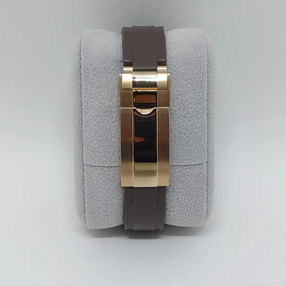 Brown leather watch strap with polished gold-tone folding clasp on gray cushion.