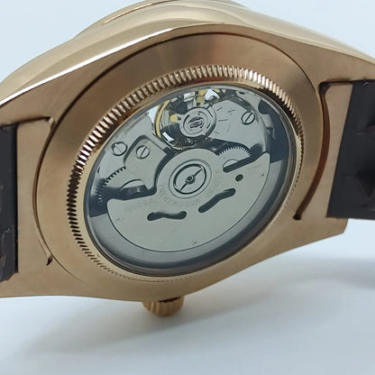 Close-up of gold-tone watch case back with visible silver mechanical movement and black leather strap.