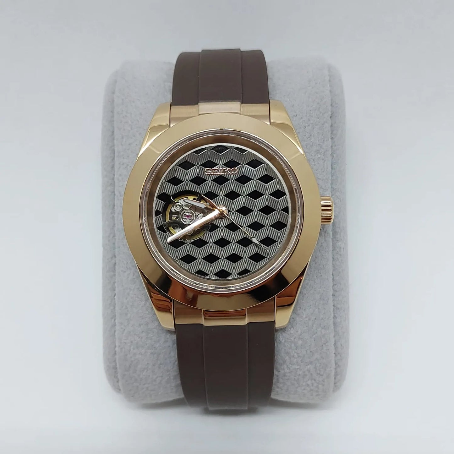 Rose gold-tone stainless steel watch with brown rubber strap and black guilloche patterned dial.