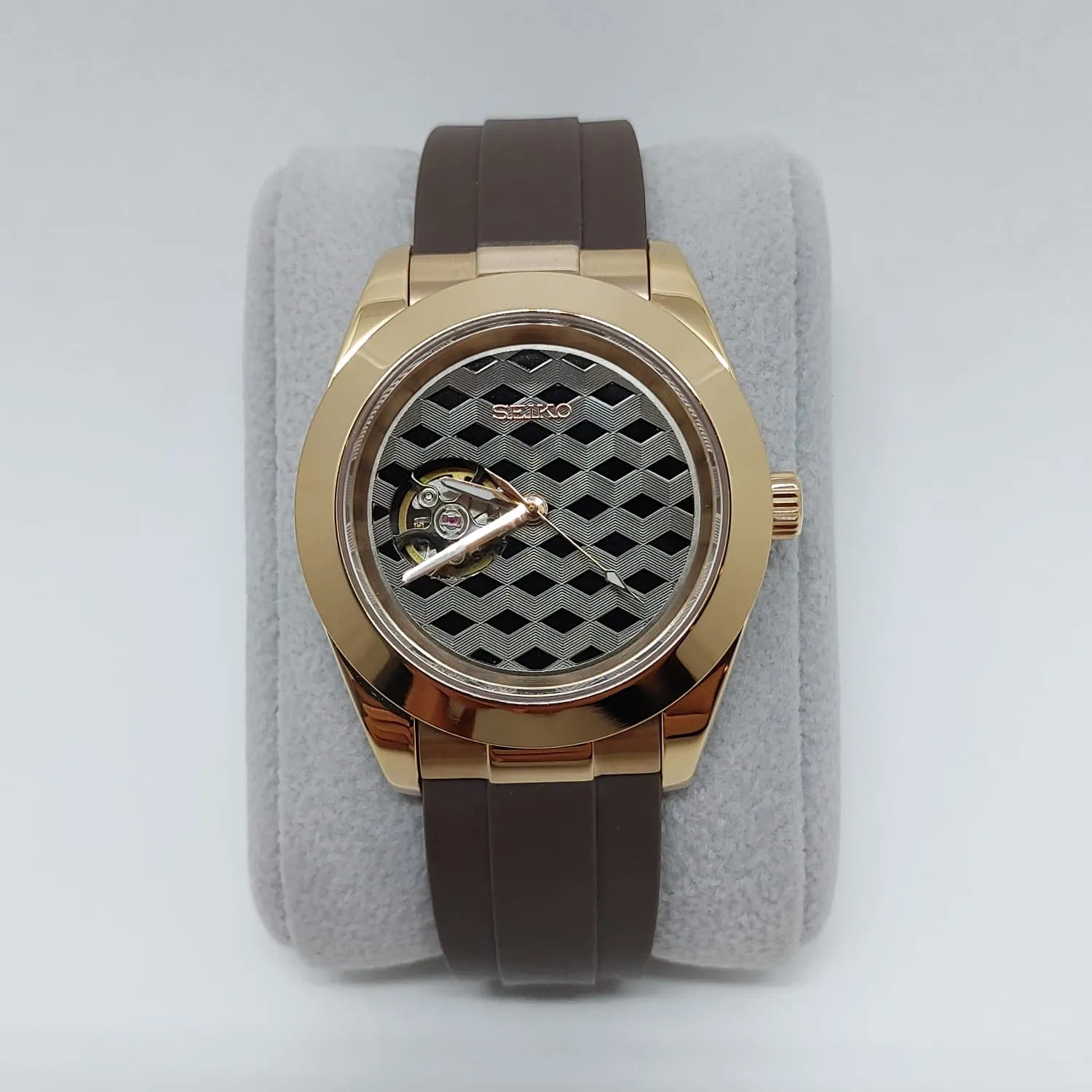 Rose gold-tone stainless steel watch with brown rubber strap and black guilloche patterned dial.