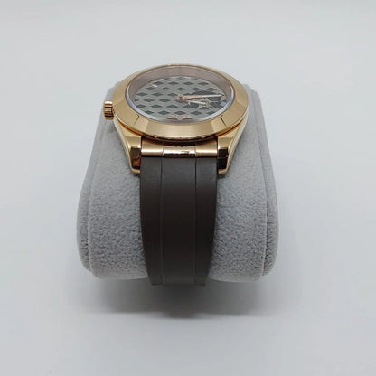 Gold-toned round watch with textured Guilloche dial and dark brown rubber strap on gray cushion.