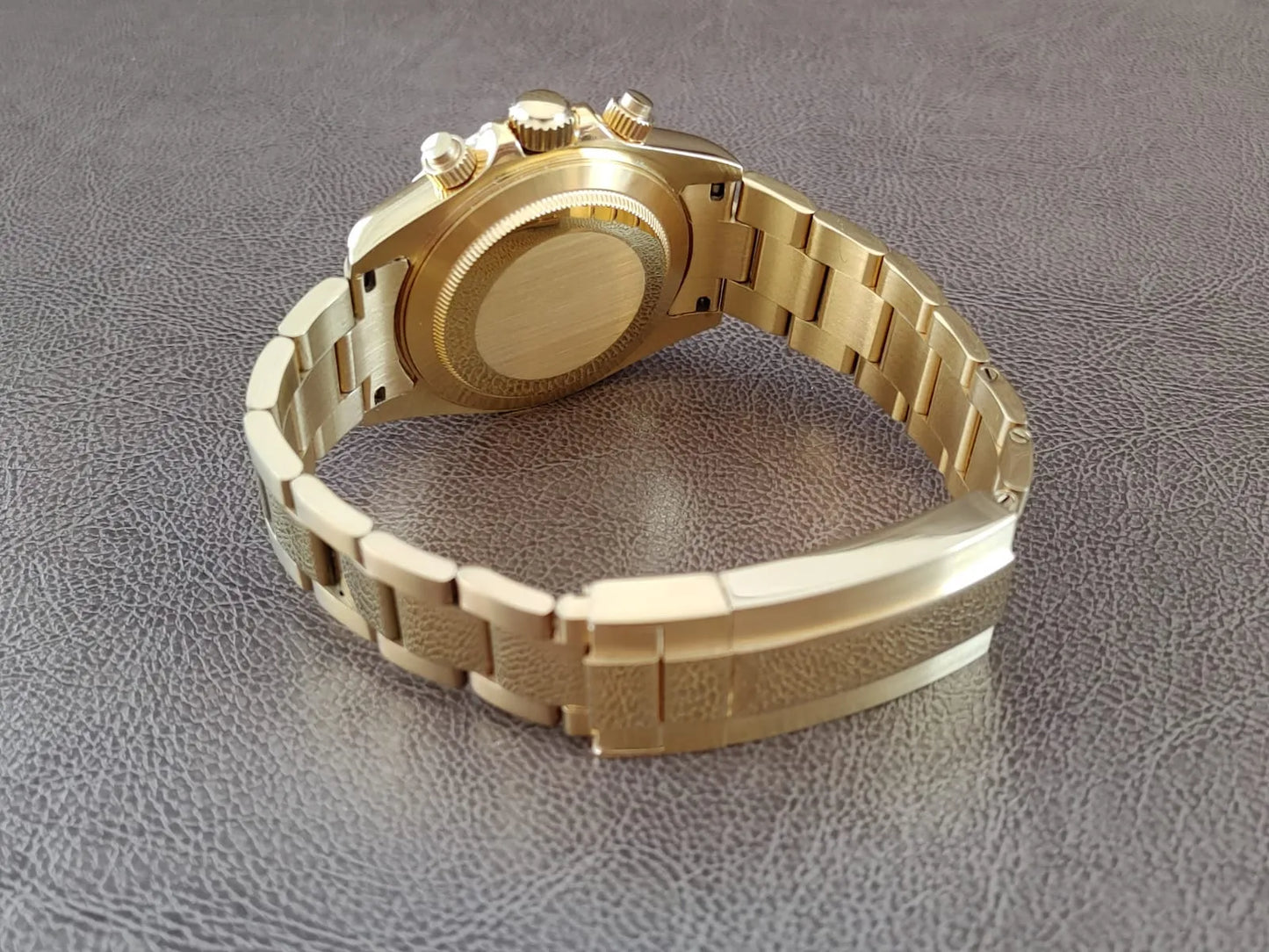 Gold-tone stainless steel watch with polished bracelet and closed case back on textured surface.