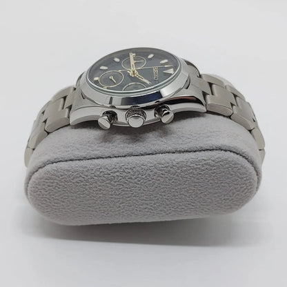 Stainless steel chronograph watch with black dial, cream subdials, and metal link bracelet on gray cushion.