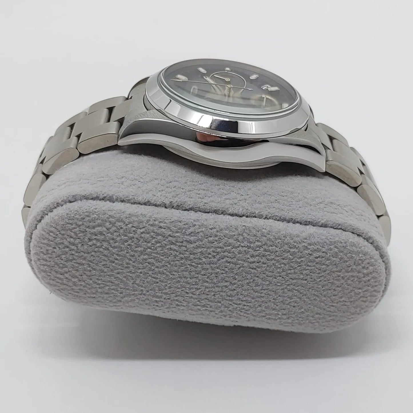 Seiko stainless steel wristwatch with black dial, silver markers, and metal link bracelet on gray cushion.