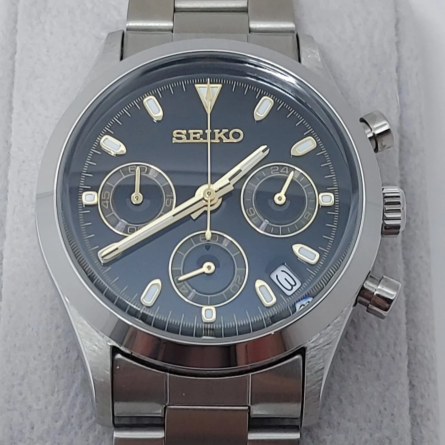 Seiko VK63 chronograph watch with black dial, gold-tone markers, three subdials, date window, and stainless steel bracelet.