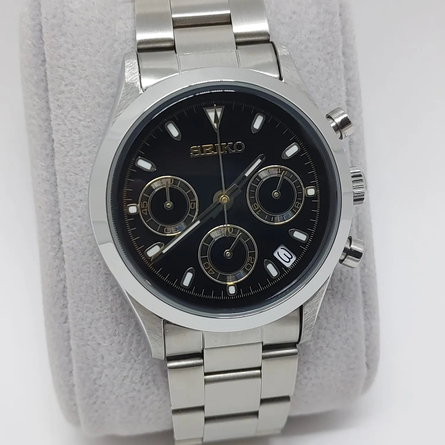 Seiko VK63 chronograph wristwatch with black dial, gold accents, three subdials, date display, and stainless steel bracelet.