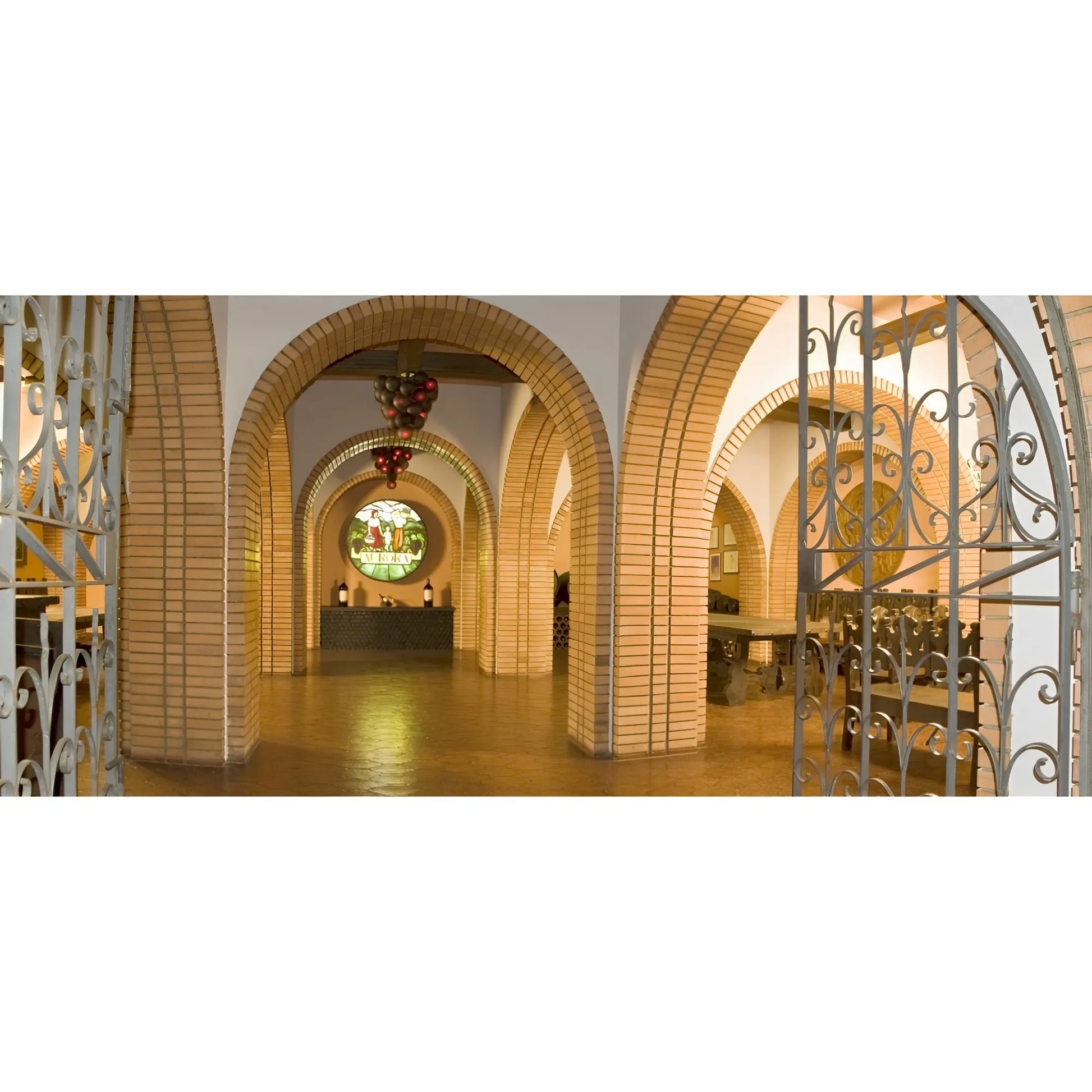 Brick archway corridor with wrought iron gates and a decorated chandelier in a warm, softly lit cellar.