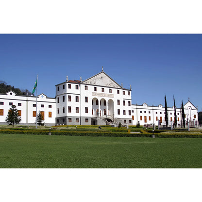 Large white historical mansion with red roof tiles under clear blue sky, surrounded by manicured green lawn.