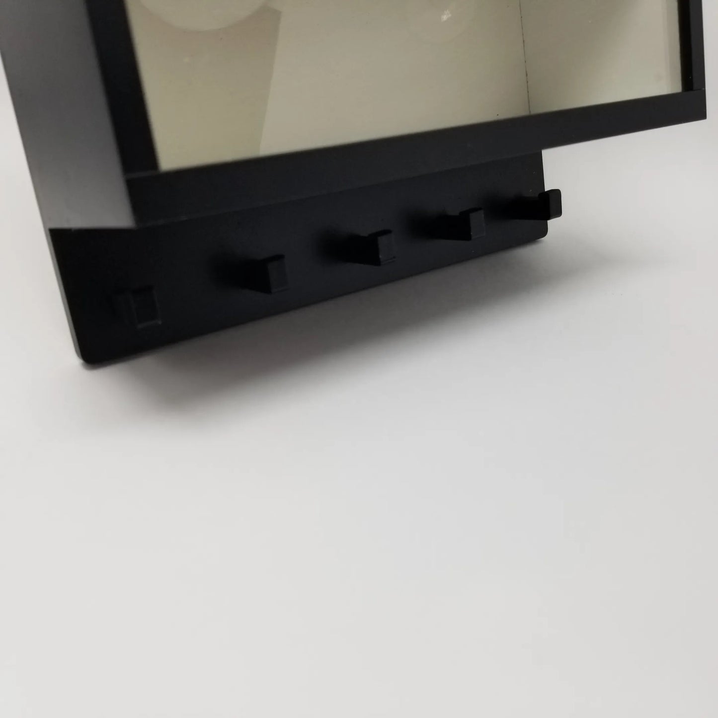 Black metal wall key hook rack with four evenly spaced hooks, attached to a clear display case frame.