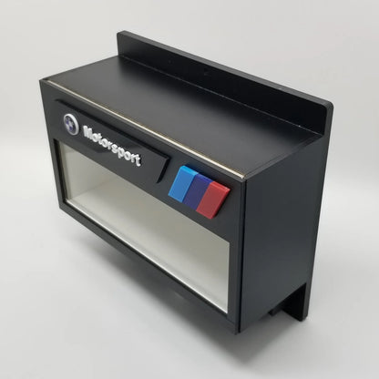 Black BMW Motorsport wall-mounted key hook rack with glass display case and red, blue, and purple stripes.