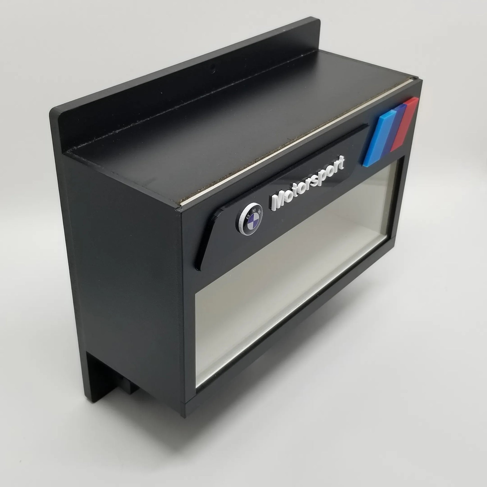 Black wall-mounted key hook rack with BMW Motorsport logo and red, blue, and light blue stripes, designed to hold scale.