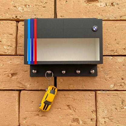 Black BMW wall key hook rack with clear display case, red and blue racing stripes, and five metal hooks holding a yellow.
