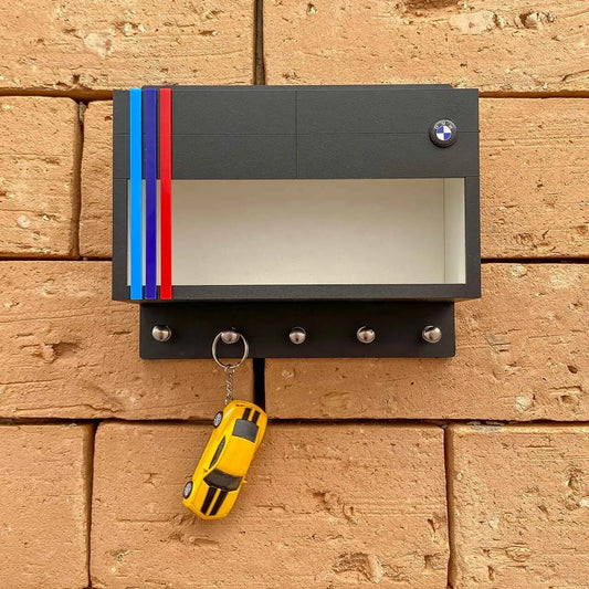 Black BMW wall key hook rack with clear display case, red and blue racing stripes, and five metal hooks holding a yellow.