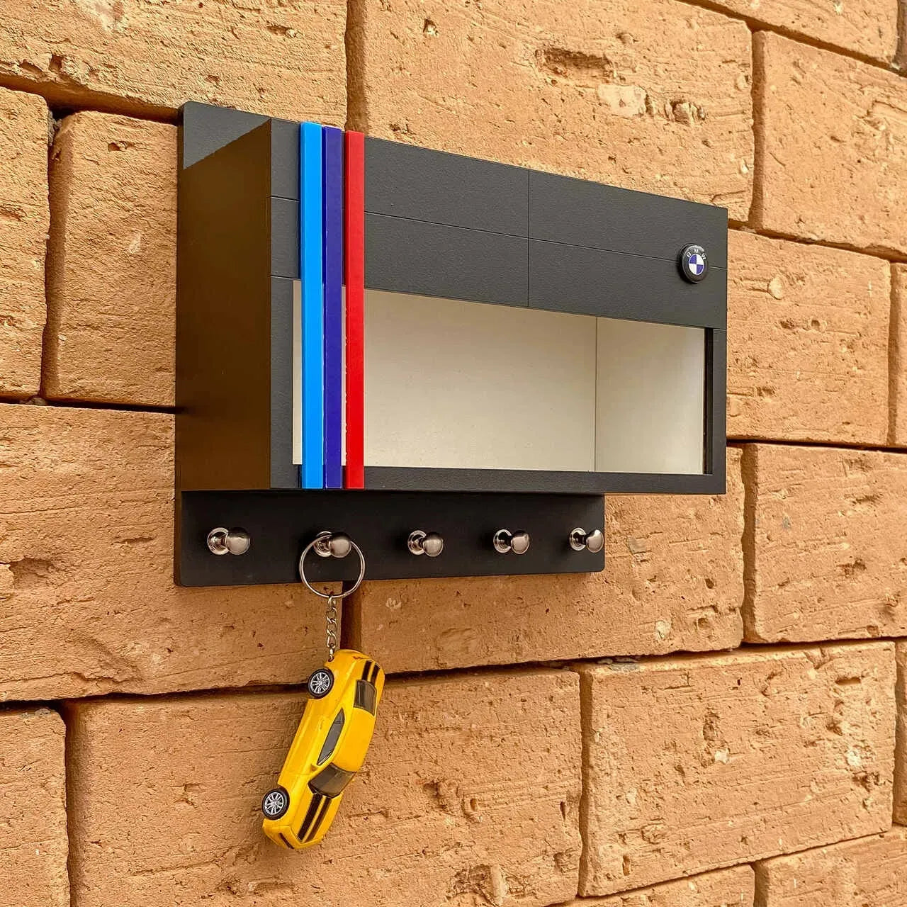 Black rectangular wall key hook rack with BMW logo, red and blue stripes, five metal hooks, and a mirror panel.