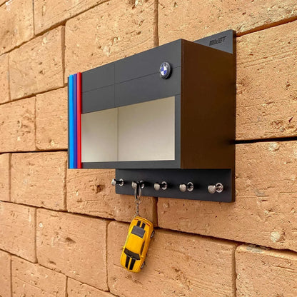 Black rectangular wall-mounted key hook rack with BMW logo, three metal hooks, and a miniature yellow car keychain hanging.