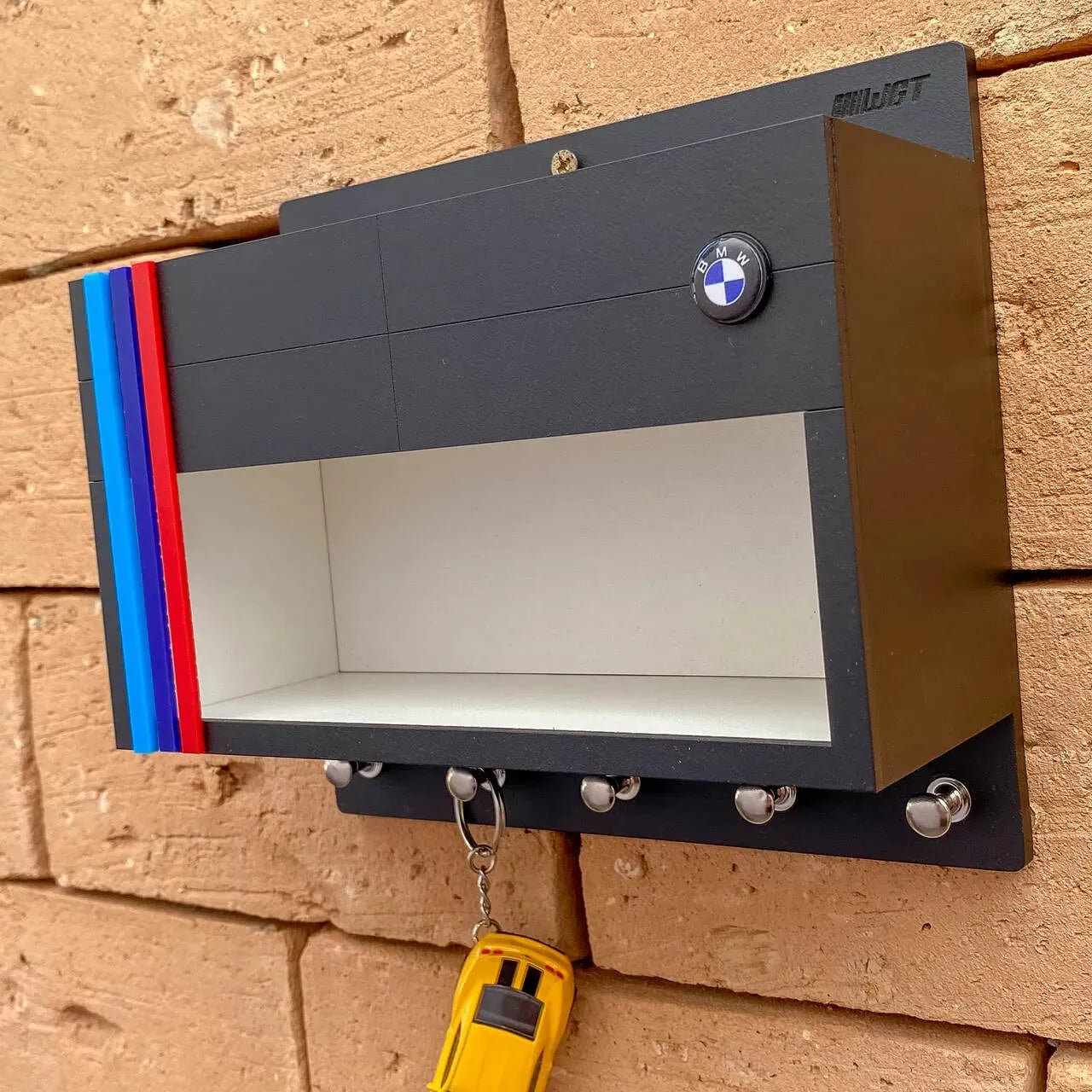 Black wall-mounted key hook rack shaped like a BMW garage with blue, red, and dark blue stripes and BMW logo on top.