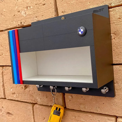 Black wall-mounted key hook rack shaped like a BMW garage with blue, red, and dark blue stripes and BMW logo on top.