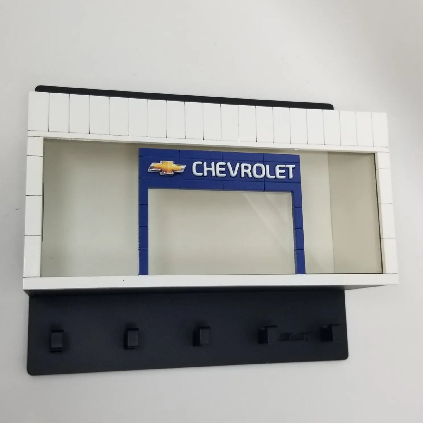 Black wall-mounted key hook rack featuring a white and blue Chevrolet scale model car display case.