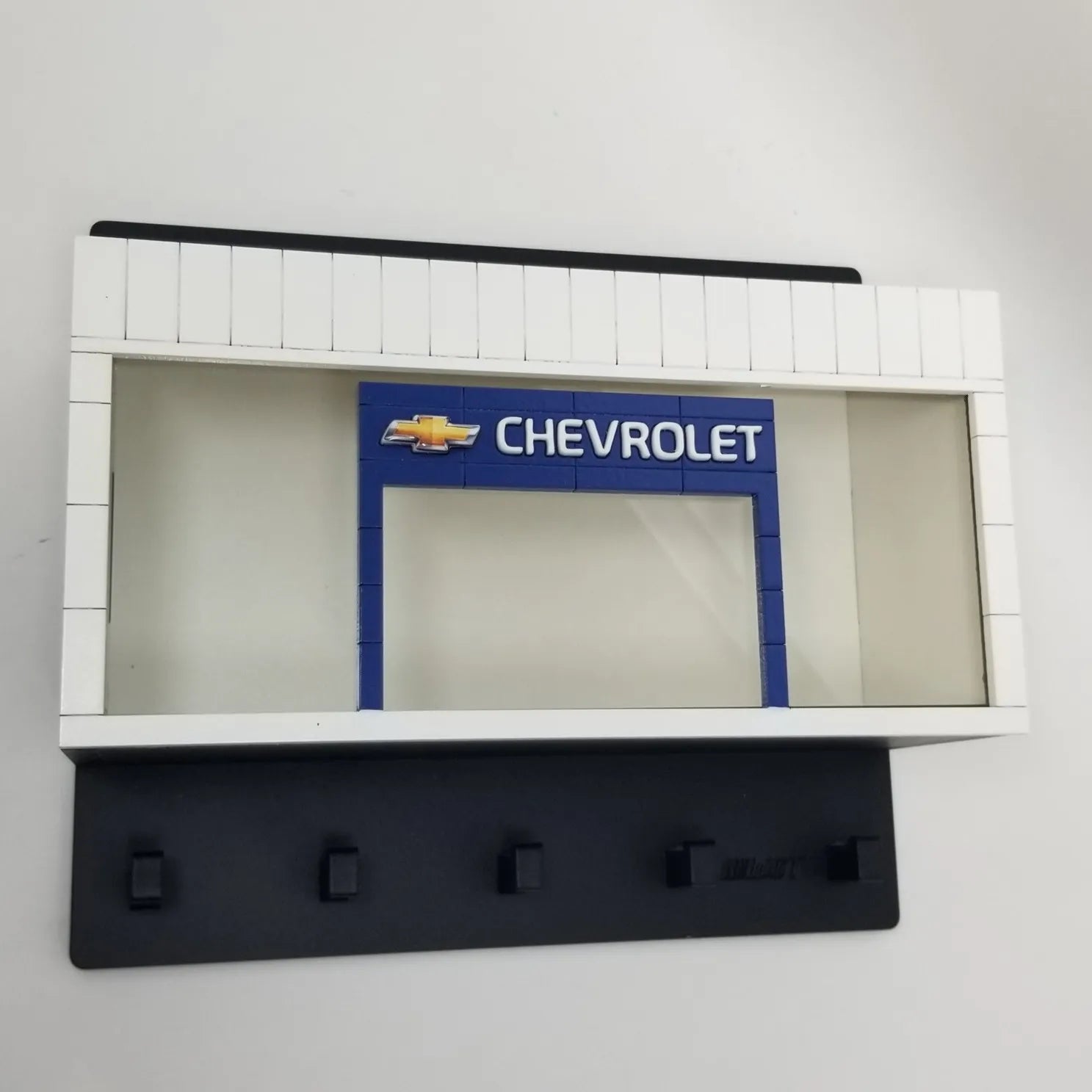Black wall-mounted key hook rack featuring a white and blue Chevrolet scale model car display case.