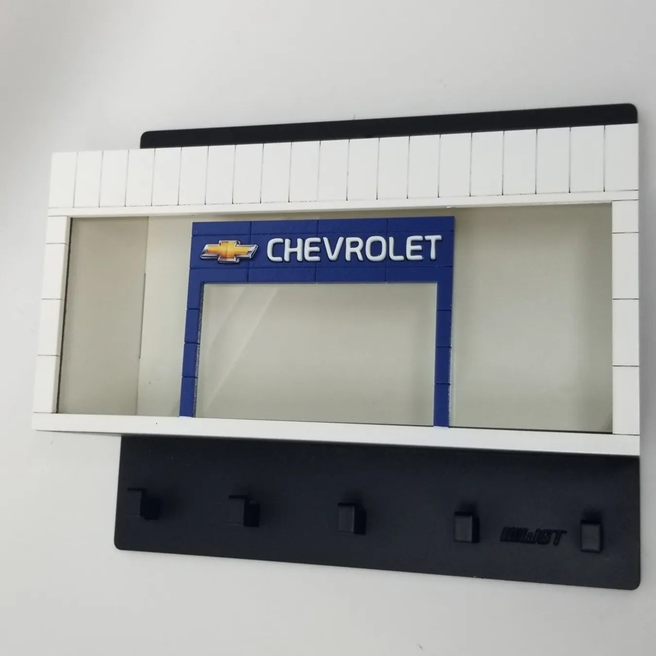 White and black wall-mounted key hook rack with Chevrolet logo and four black hooks.