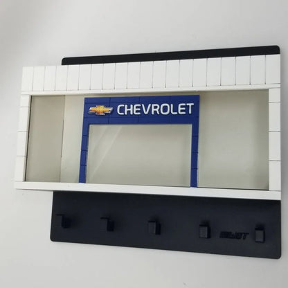 White and black wall-mounted key hook rack with Chevrolet logo and four black hooks.