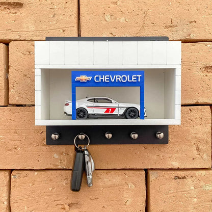 Black and white Chevrolet wall key hook rack with silver hooks and a scale model car inside a display case.