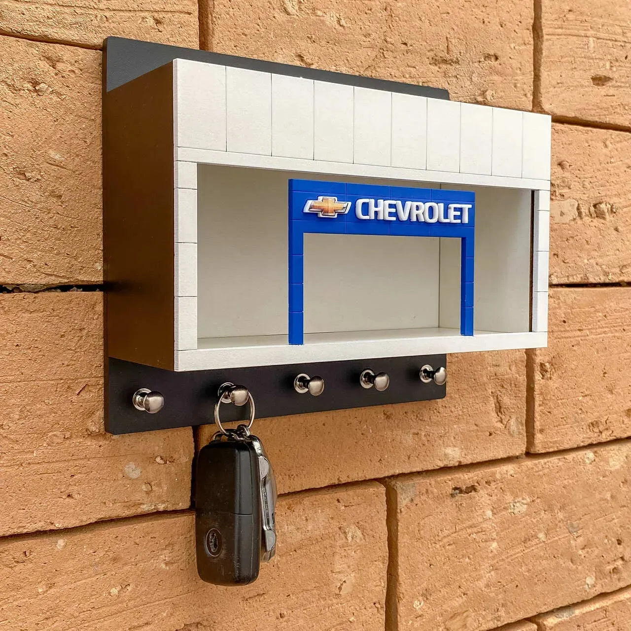 Black and white Chevrolet wall-mounted key hook rack with silver hooks and a display case with Chevrolet logo.