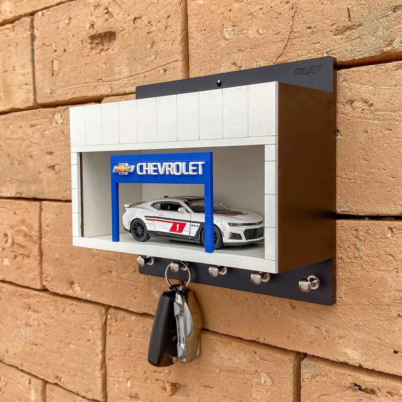 Black and white rectangular wall key hook rack with silver hooks and a miniature white Chevrolet car inside a display case.