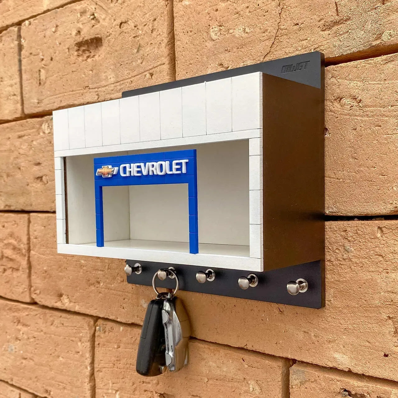 Black and white Chevrolet wall-mounted key hook rack with silver hooks and a blue scale model car display slot.