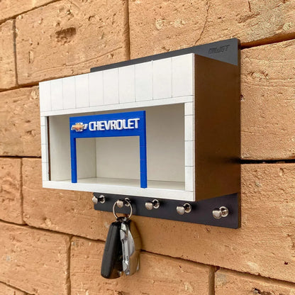 Black and white Chevrolet wall-mounted key hook rack with silver hooks and a blue scale model car display slot.