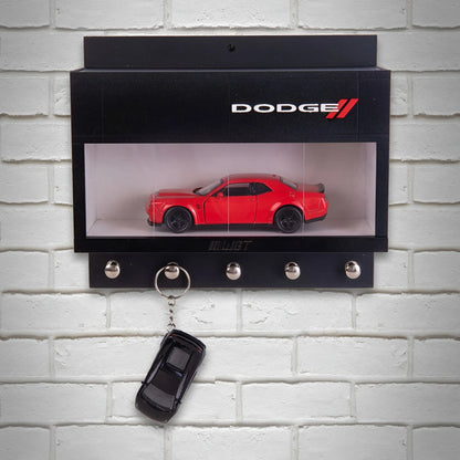 Black wall-mounted key hook rack with clear display case holding red Dodge model car and three metal hooks, one with a.