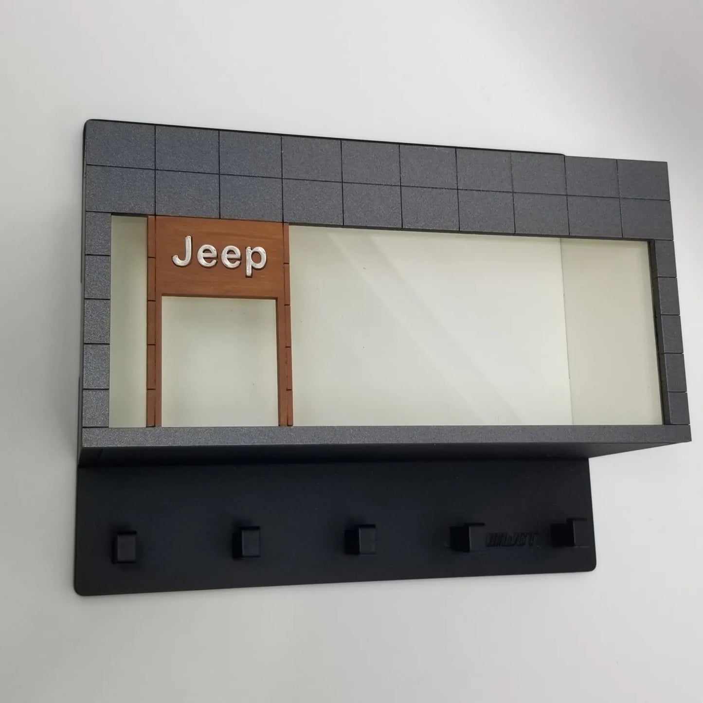 Black wall-mounted key hook rack with five hooks and gray frame featuring a Jeep scale model car display case.