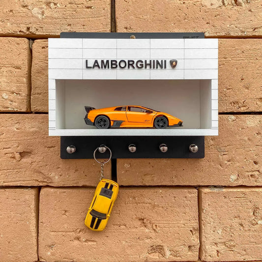 White wall-mounted key hook rack shaped like a Lamborghini showroom with an orange scale model car and five metal hooks below.
