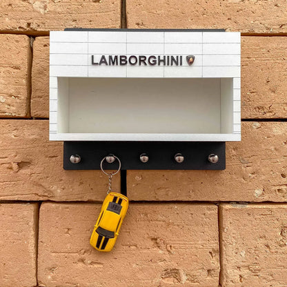 White and black wall-mounted key hook rack with Lamborghini logo and five metal hooks, holding a yellow car-shaped keychain.