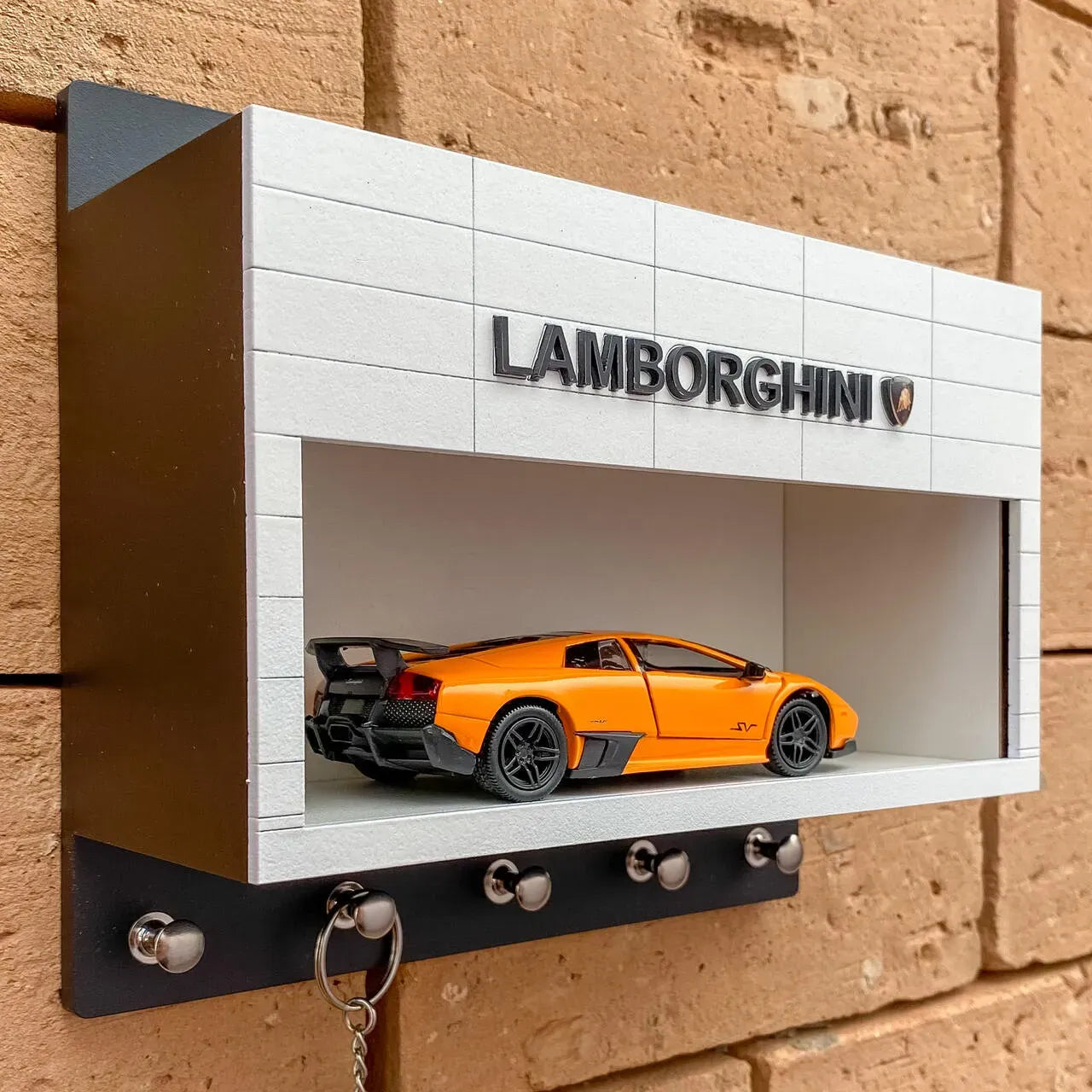 White rectangular wall-mounted key hook rack with Lamborghini logo and orange scale model car inside.