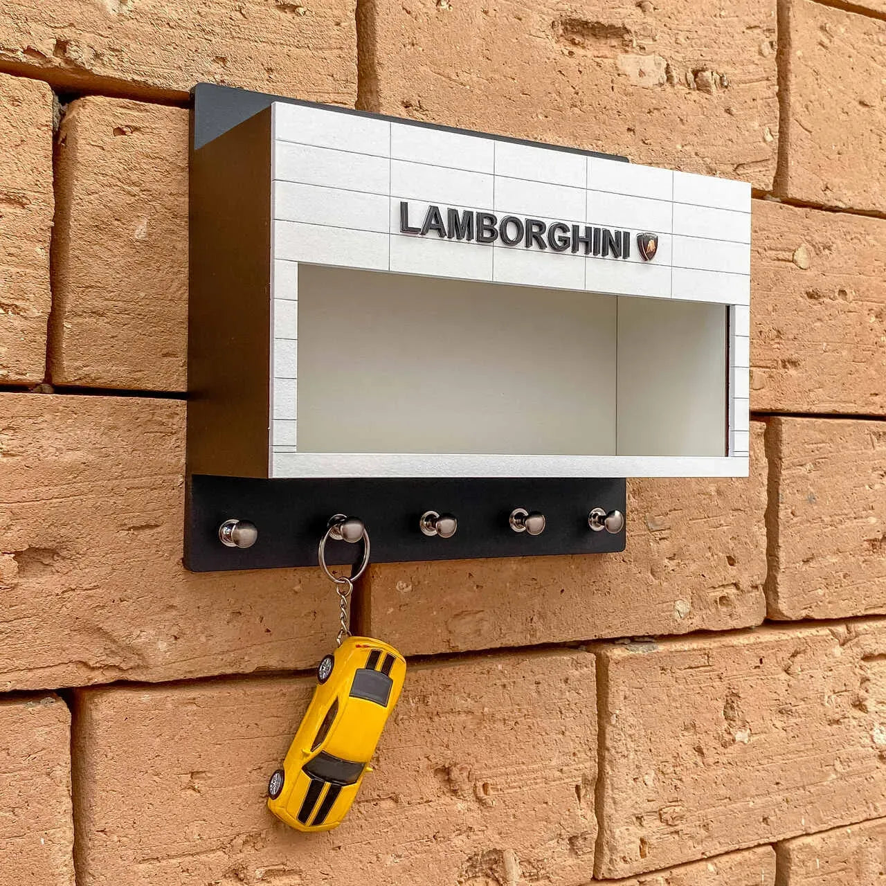 White and black Lamborghini wall-mounted key hook rack with four silver hooks and a yellow sports car keychain hanging on.