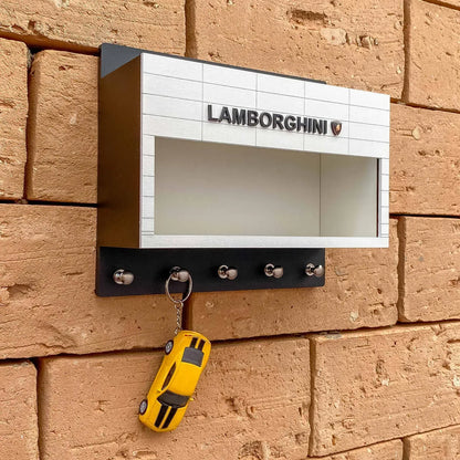 White and black Lamborghini wall-mounted key hook rack with four silver hooks and a yellow sports car keychain hanging on.