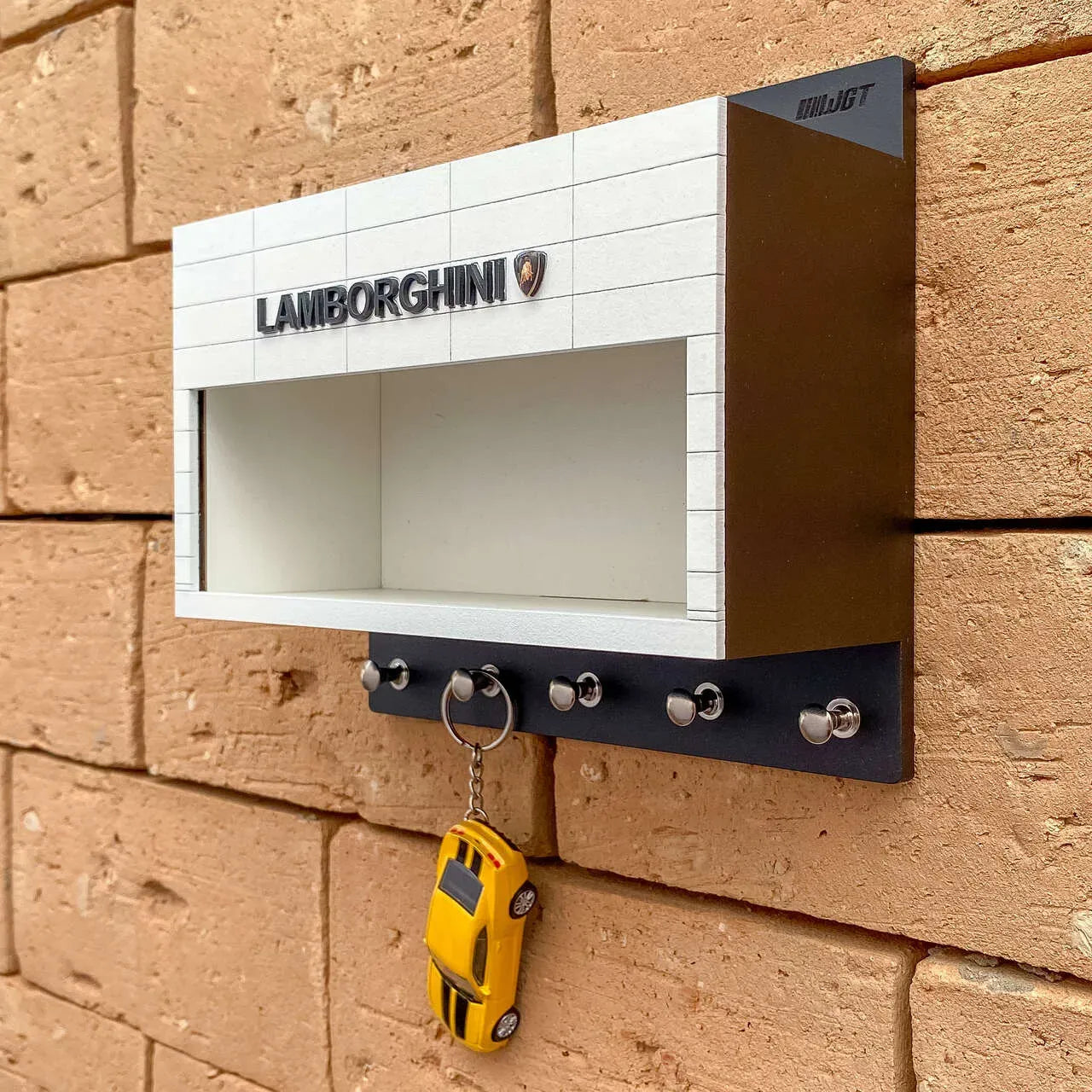 White and black wall-mounted key rack with Lamborghini logo and miniature yellow Lamborghini car keychain hanging from hooks.