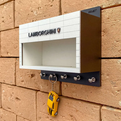 White and black wall-mounted key rack with Lamborghini logo and miniature yellow Lamborghini car keychain hanging from hooks.