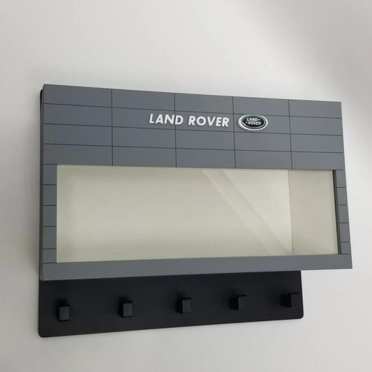 Gray Land Rover wall key hook rack with scale model car display case and five black hooks.