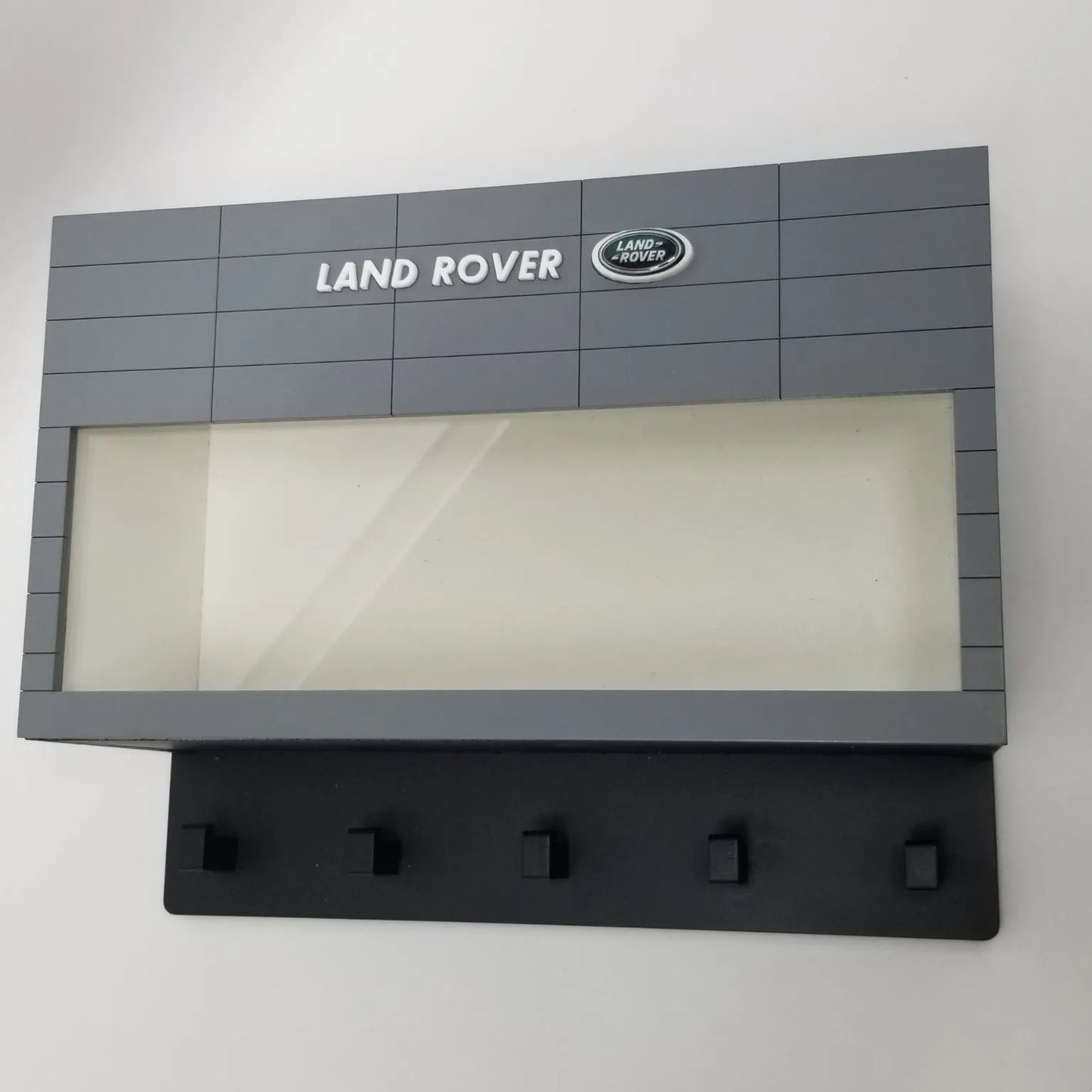 Gray and black Land Rover wall-mounted key hook rack with display case and five black hooks.