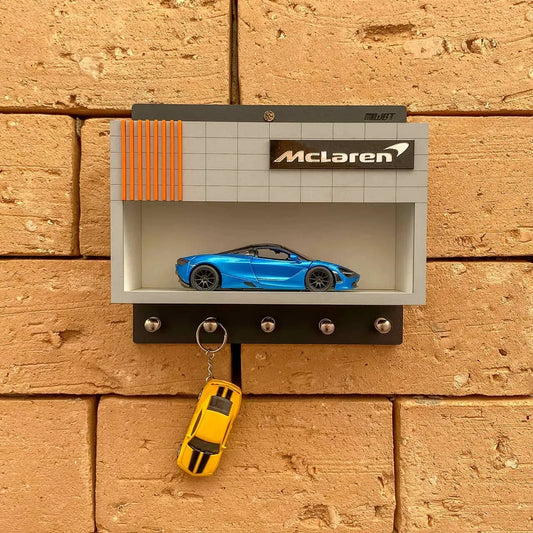Black wall-mounted key hook rack with a gray shelf, orange stripe detail, McLaren logo, and blue scale model car on display.