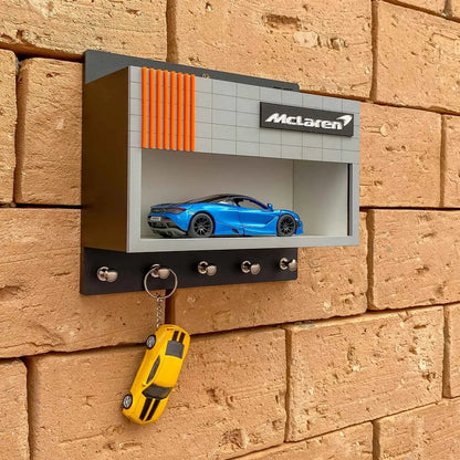 Gray and black wall-mounted key hook rack with orange stripes, featuring a blue McLaren model car inside a display case and.