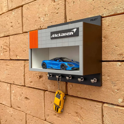 Wall-mounted black and grey metal key hook rack with McLaren logo and blue scale model car display case.