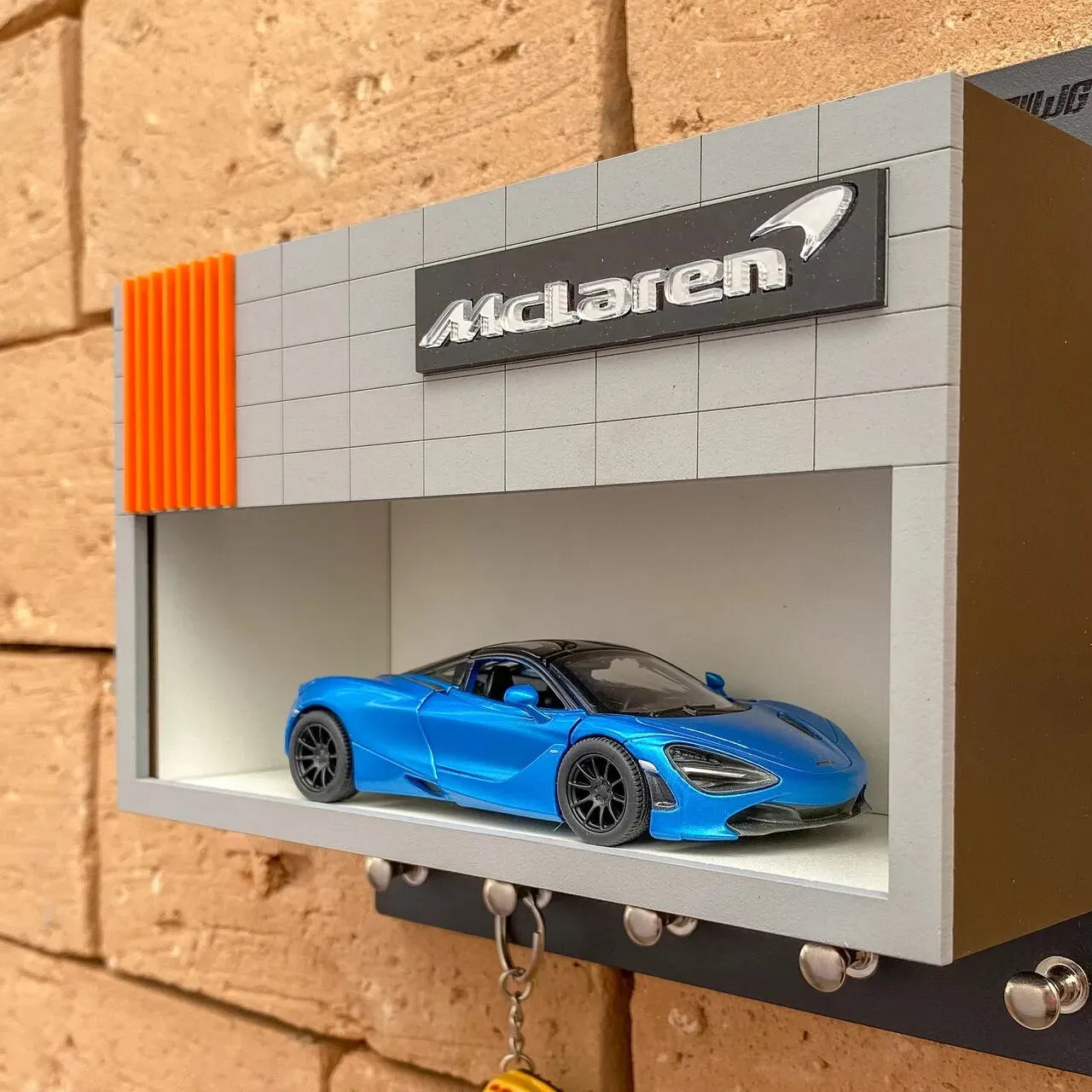 Blue McLaren model car displayed inside gray wall-mounted key hook rack with black hooks and orange accents.