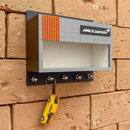 Wall-mounted gray and orange McLaren key hook rack with four metal hooks and empty display shelf above.