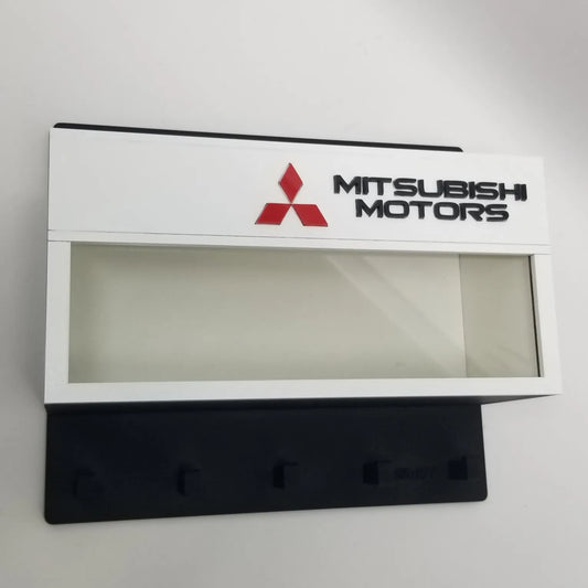 White rectangular Mitsubishi Motors wall key hook rack with clear display case and four black hooks.