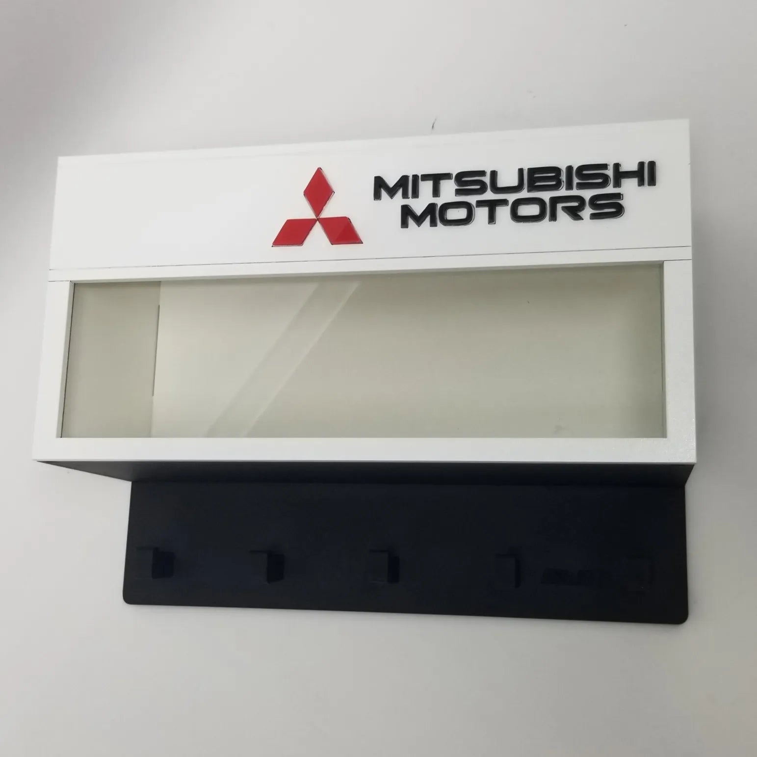 White Mitsubishi Motors wall key hook rack with red logo and four black hooks.